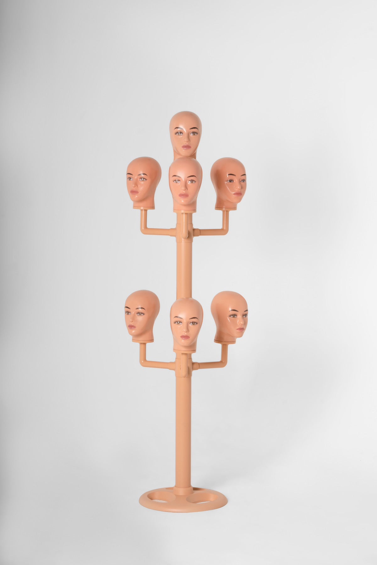 The wig hanger with 7 bald heads in a white backdrop.