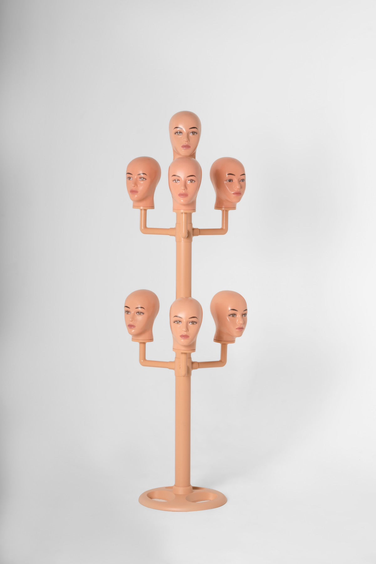 The wig hanger with 7 bald heads in a white backdrop.
