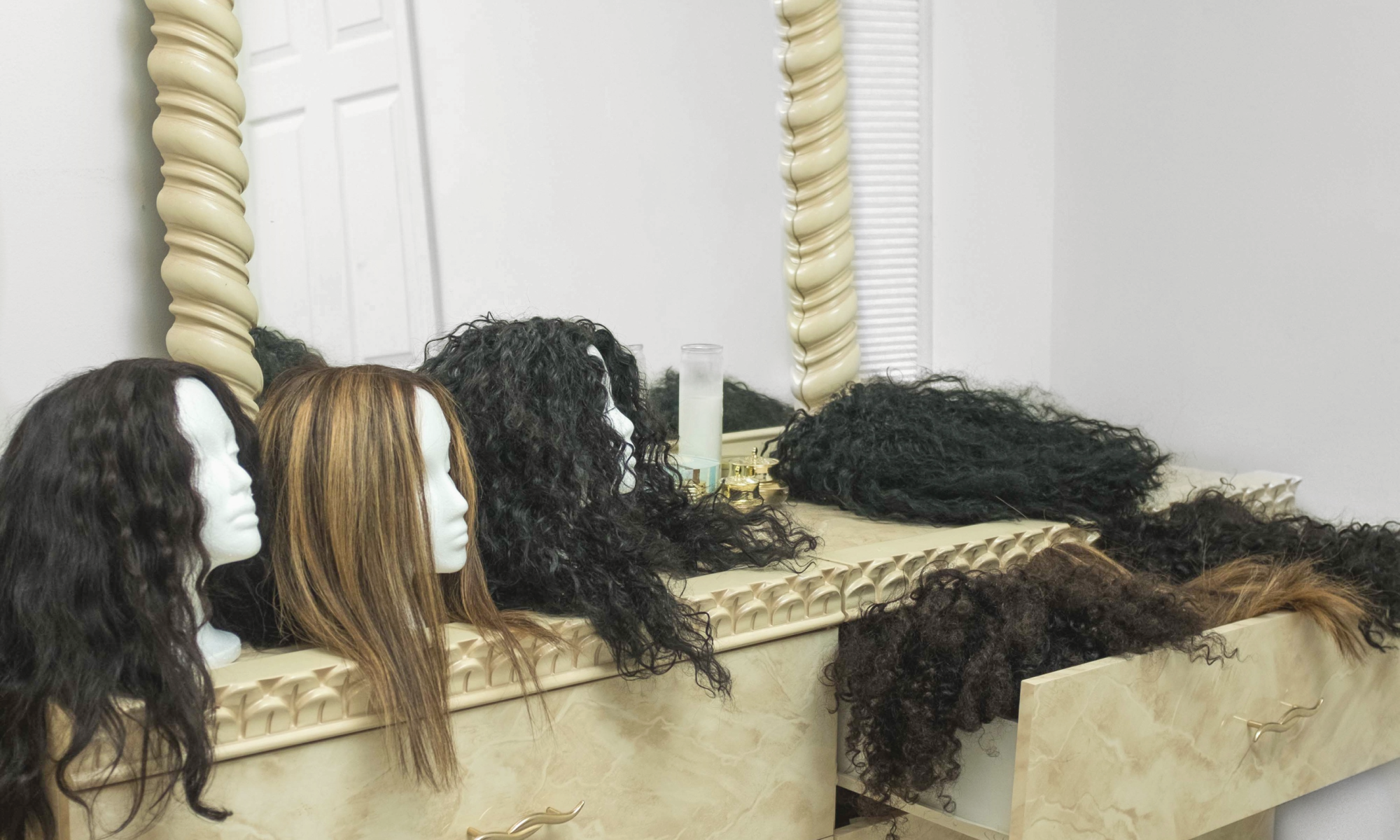 Multiple wig randomly laid out across the counter of a dresser.